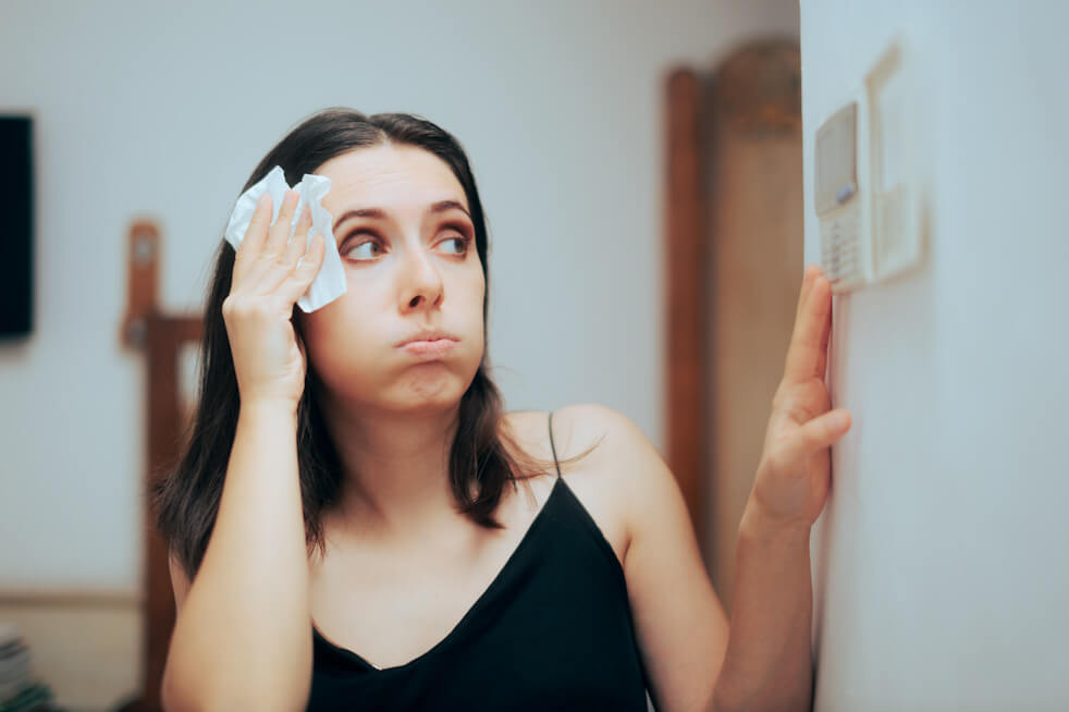 woman looking at thermostat in hot house